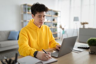 Focused asian man working on laptop and writing